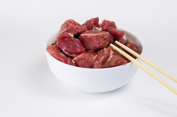 Ceramic bowl with raw marinated meat and bamboo sticks on a whit