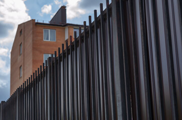 Apartments behind a high fence against a blue sky with clouds. T