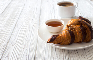 Croissant with chocolate on white plate and cup of coffee close up