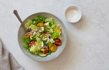 Mixed salad leaves, red and yellow tomatoes, cucumber and red onions salad in rustic bowl