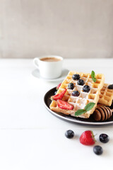 Waffles plate on table with blueberry, strawberry, mint and white cup of coffee