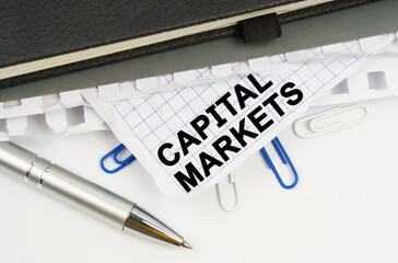 On the table is a pen, notebooks and a crumpled sheet of paper with the inscription - CAPITAL MARKETS