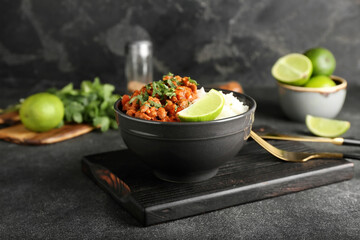 Bowl with tasty chili con carne, rice and lime on dark background