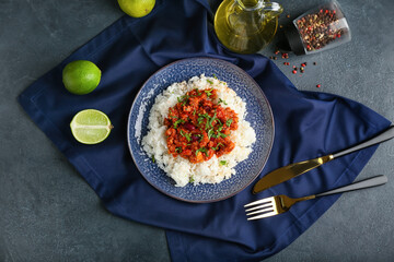 Plate with tasty chili con carne, rice and lime on dark background