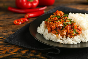 Plate with tasty chili con carne, rice and vegetables on wooden background, closeup