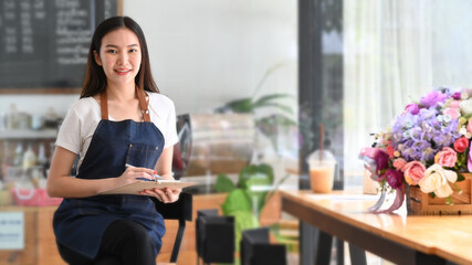 Female coffee shop owner holding note pad and smiling to camera.