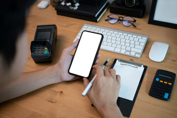 Over shoulder view of man using mobile phone and making note on notebook.