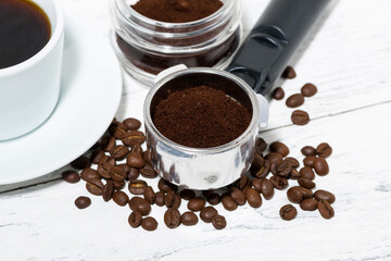holder with ground coffee and cup of coffee on white background, top view