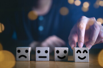 Businessman hand holding touching smile face or happy face which print screen on wooden cube block, Business service rating , Satisfaction concept.Selection & Choosing emotion or mood concept.
