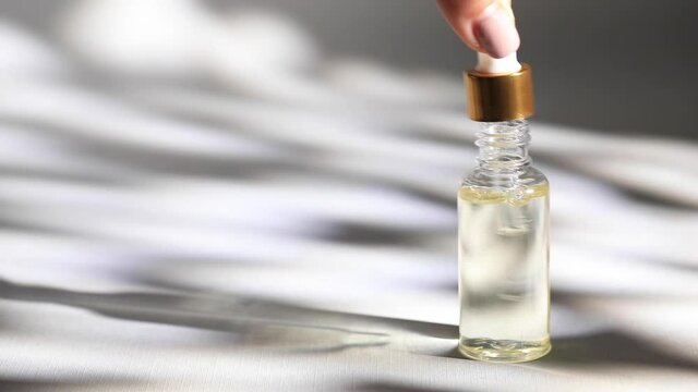 Mockup of a glass dropper bottle. An oily drop falls from the cosmetic pipette