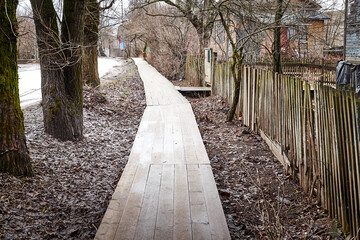 A wooden sidewalk goes through muddy wet countryside road. A path on wet clay.