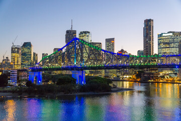 Colourful lights from a large bridge and city skyline reflected in a river at sunset