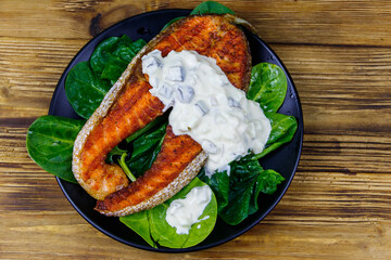 Grilled salmon steak with spinach and tartare sauce on wooden table. Top view