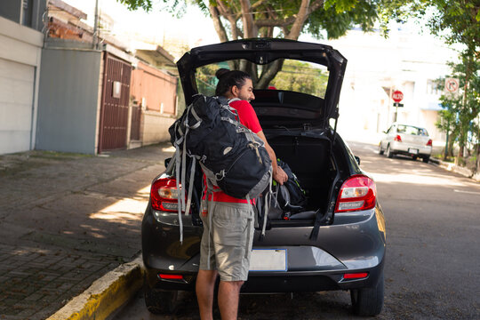 Man carrying a suitcase into the trunk of the car, ready to go on a trip