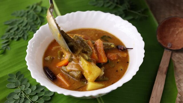 Sambar , serving Lentil sambar mixed vegetable curry soup for Onam sadhya vishu spicy hot isolated green banana leaf. popular south Indian food Kerala Tamil Nadu Sri lanka 4K slow motion video footage