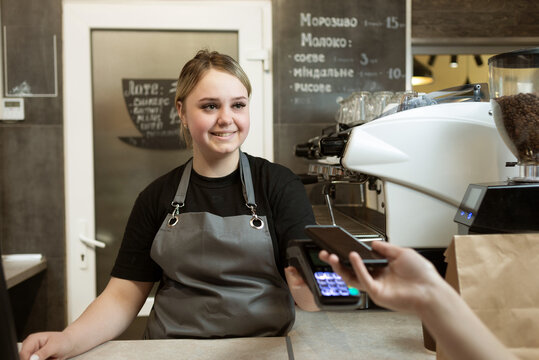 The client pays by phone for the order in the cafe to the seller for the girl through the payment nfs terminal. Small business selling coffee and drinks. Contactless payment.