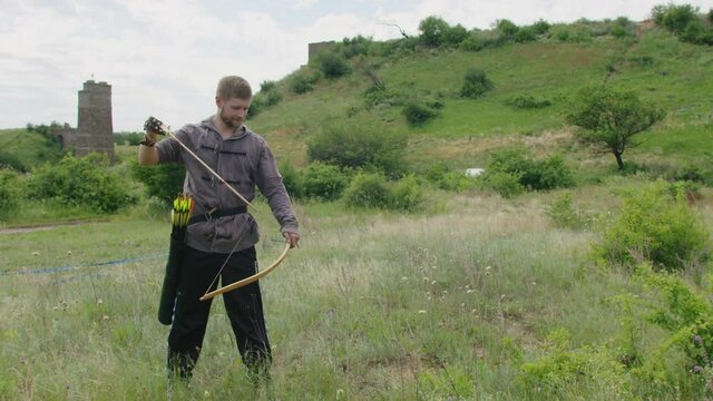 a young guy shoots a bow at a target, in nature, and hits the target, the arrow pierces the target for flight, pulls the bowstring tightly for a shot. Prores 422