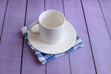 White empty cup and saucer, kitchen cotton napkin on colored background, close-up. Concept of breakfast, afternoon tea. Top and side view.