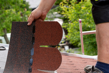 Roofer hands installing bitumen roof shingles using hammer in nails. Installation of waterproofing...