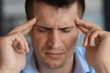 Portrait of young caucasian man, massaging touching temples having severe headache or migraine, close up