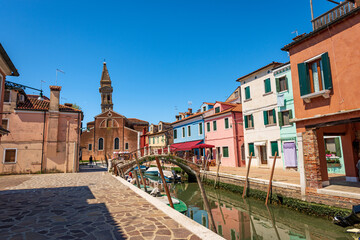 Burano island, multi colored houses, small canal with moored boats and the Parish church of San Martino Vescovo (Saint Martin Bishop) with the leaning bell tower (XVI century), Venice, Veneto, Italy.