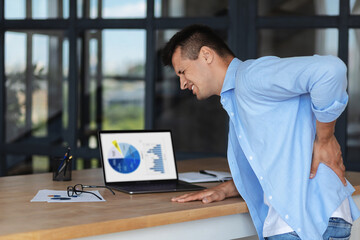 Young caucasian businessman feeling severe backache from a long sedentary work at the computer in...