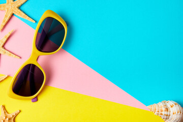 Sunglasses on minimal colorful background decorated with starfish and exotic sea shells with copy space