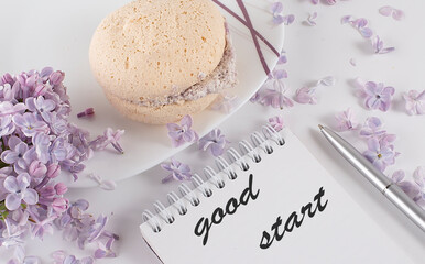 an open notebook with and lilac flowers on a desk and biscuits and text GOOD START