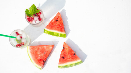 Watermelon slices, on a white wooden background. Next to it is a cocktail with pomegranate seeds in a glass. Place for the text. View from the top.