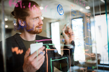 Young man working with datas and diagrams, writing ideas on glass office wall