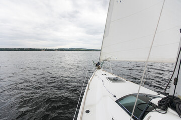 Fototapeta premium River boat trip. Details on a sailing yacht. We go by boat in the summer. White yacht with full sails running downwind wing-on-wing, sailing after the storm. Leisure activity, sport, recreation theme.