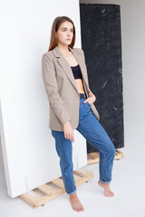 portrait of young attractive caucasian woman with long brown hair in suit jacket. skinny pretty lady posing in front of studio flag with bare feet. model tests of beautiful female