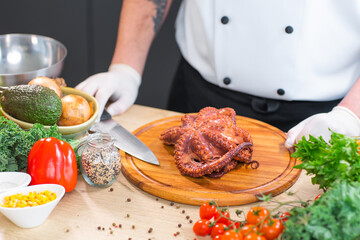 Young chef is cutting octopus in a modern kitchen. The man prepares food at home. Cooking healthy and tasty food.