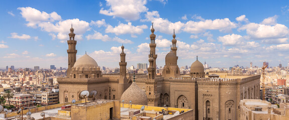 Aerial day shot of minarets and domes of Sultan Hasan mosque and Al Rifai Mosque mediating shabby buildings with satellite dishes in cloudy day, Old Cairo, Egypt - obrazy, fototapety, plakaty