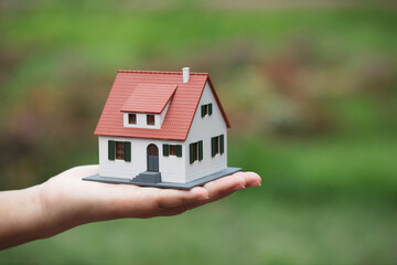 Hand holding small house in front of green background