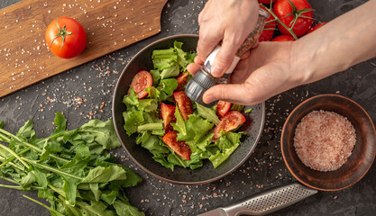 Women's hands are sprinkling a light vitamin vegetable salad with spices. Concept of cooking healthy food. Top view and dark background