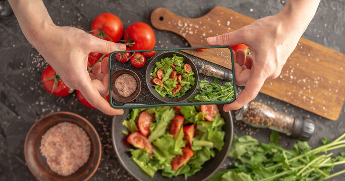 Women's hands are holding a mobile phone over a beautiful appetizing vegetable salad to take a photo