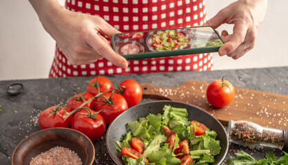 Women's hands are holding a mobile phone over a beautiful appetizing vegetable salad to take a photo