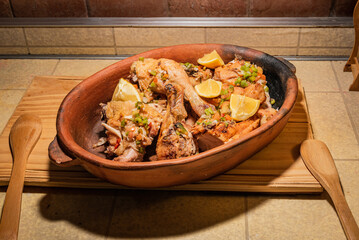 Homemade grilled chicken with spices cut into pieces in red ceramic baking dish on wooden board.