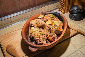 Homemade grilled chicken with spices cut into pieces in red ceramic baking dish on wooden board.