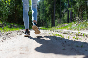 Obraz premium Rear view photo of female tourist legs walking in a forest road.Summer day.