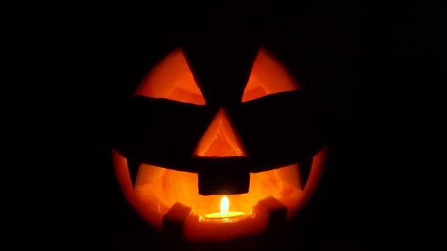 Close-up of Jack lantern. Scary face is carved into orange pumpkin. One candle burns inside the vegetable. Halloween night.