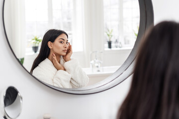 Young asian woman sitting in front of mirror touching face
