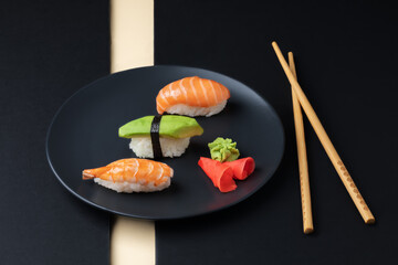 Japanese cuisine - set of nigiri sushi with salmon, avocado ans schrimp on a black plate with chopsticks.