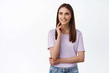Image of young smiling woman, looking with interest, determined, made her decision, staring left with pleased, satisfied face expression, standing against white background