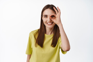 Zero problems. Smiling brunette girl shows okay OK sign over eye, pleased and praise thing,...