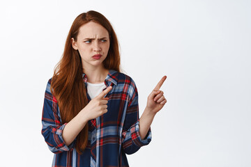 Wtf. Confused redhead woman pointing and looking right with cringe and disgust, stare at something...