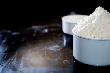 Close-up of dessert preparation with flour being mixed in a plastic cooking cup on a black textured...