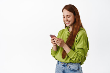 Technology. Redhead teenage girl smiling and reading smartphone, communicating via mobile app,...