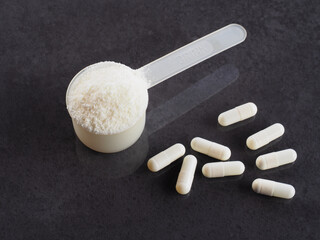 Protein powder, capsules, chondroitin, glucosamine in a plastic spoon for making a high-calorie drink on a dark background, closeup, flat layout. Healthy sports nutrition for fitness